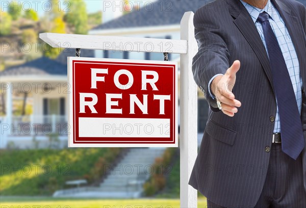 Male agent reaching for hand shake in front of for rent sign and house