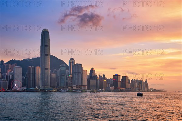 Hong Kong skyline cityscape downtown skyscrapers over Victoria Harbour in the evening with junk tourist ferry boat on sunset with dramatic sky. Hong Kong