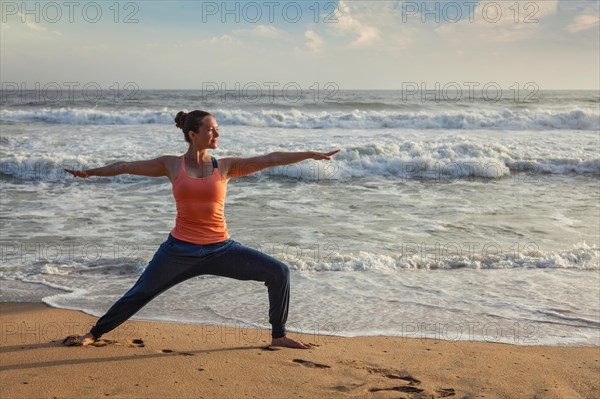 Woman doing Hatha yoga asana Virabhadrasana 1 Warrior Pose outdoors on ocean beach on sunset. Kerala