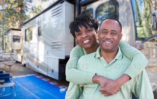 Happy african american couple in front of their beautiful RV at the campground