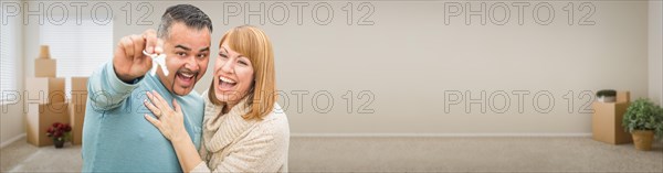 Young adult couple inside room with boxes holding new house keys banner