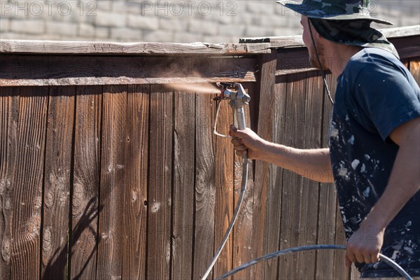 Professional painter spraying house yard fence with wood stain