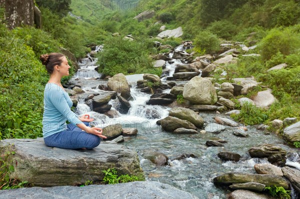 Woman in Hatha yoga asana Padmasana outdoors at tropical waterfall