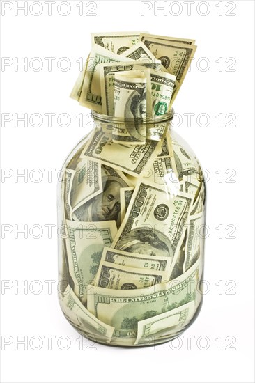 Glass jar full of hundreds of dollars isolated on white background
