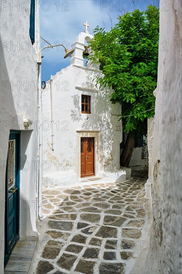 Picturesque scenic narrow Greek streets with traditional whitewashed houses with blue doors windows of Mykonos town and orthodox church in famous tourist attraction Mykonos island