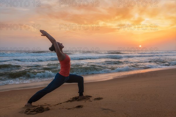 Woman doing Hatha yoga asana Virabhadrasana 1 Warrior Pose outdoors on ocean beach on sunset. Kerala