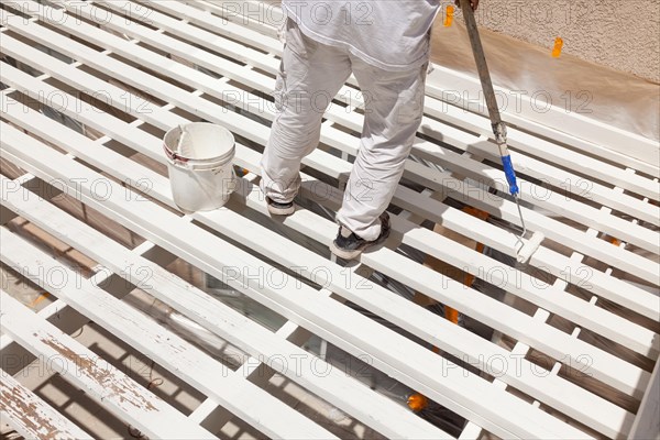 Professional painter rolling white paint onto the top of A home patio cover