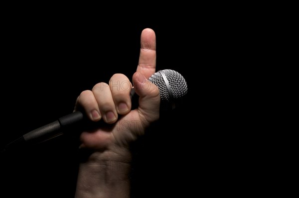 Microphone clinched firmly in male fist with index finger pointing up