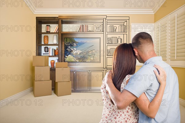 Young military couple looking at drawing of entertainment unit in room with moving boxes