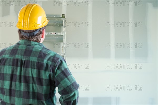 Contractor in hard hat looking at drywall