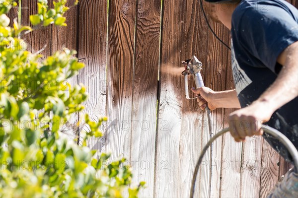 Professional painter spraying house yard fence with wood stain