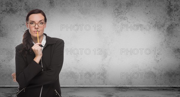 Young adult woman with pencil and glasses standing in front of blank grungy blank wall with copy space