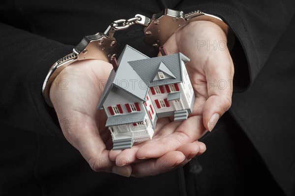 Woman in handcuffs holding small house against black