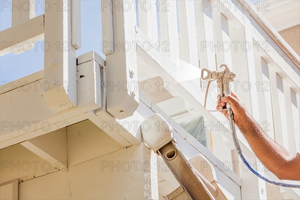 Professional house painter wearing facial protection spray painting deck of A home