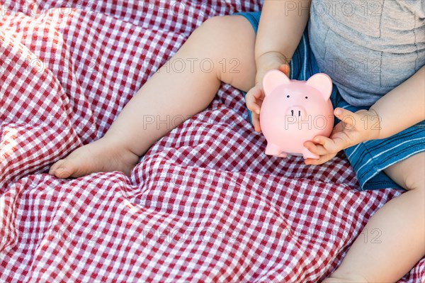 Baby boy sitting on picnic blanket playing with piggy bank