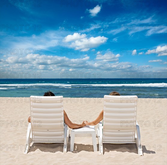 Couple in beach chairs holding hands near ocean