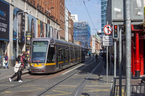 People crossing the road in the city centre with a Luas tram close by. Dublin