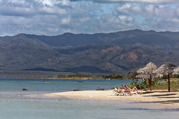 Couple lying on sun lounger on beach with parasol