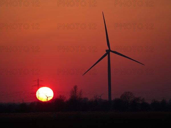 Wind turbine and high-voltage line in front of the setting sun in Hamburg's Vier- und Marschlanden. Ochsenwerder