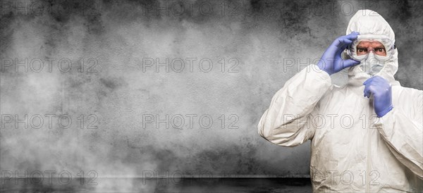 Man wearing hazmat suit and goggles in smokey room banner with copy space