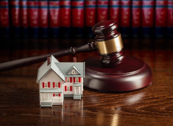 Gavel and small model house on wooden table with law books in background