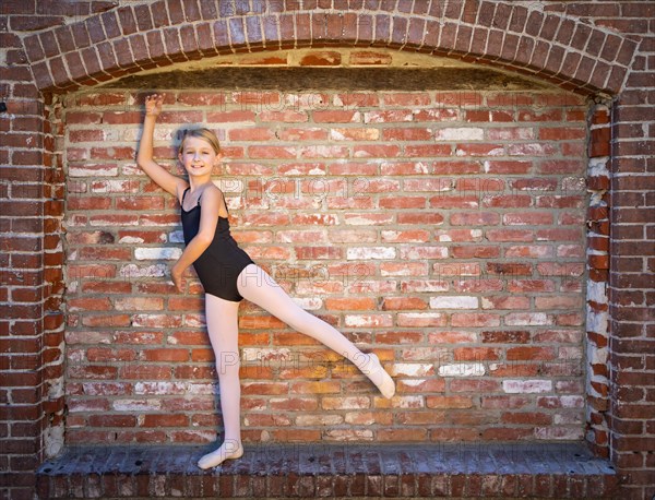 Cute caucasian ballerina girl posting against A brick wall