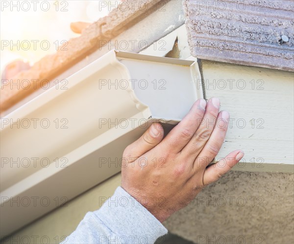 Worker attaching aluminum rain gutter to fascia of house