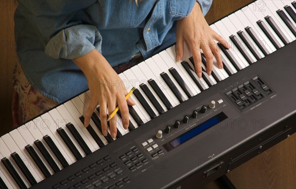 Woman's fingers with pencil on digital piano keys