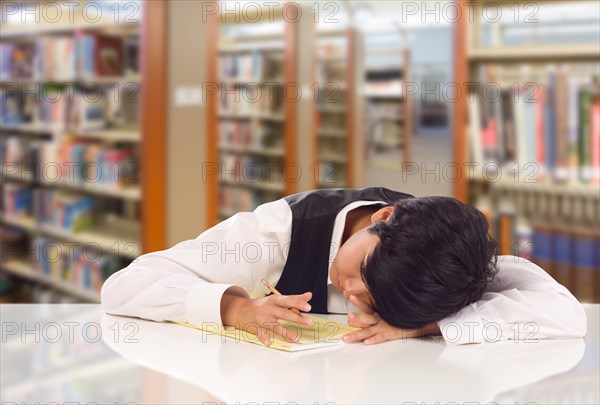 Young female mixed-race student stressed and frustrated in library with blank pad of paper