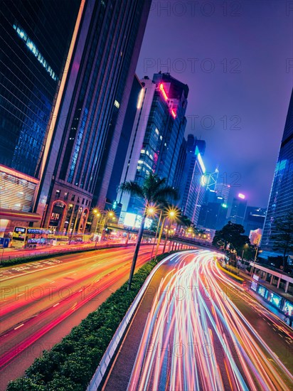 Street traffic in Hong Kong at night. Office skyscraper buildings and busy traffic on highway road with blurred cars light trails. Hong Kong