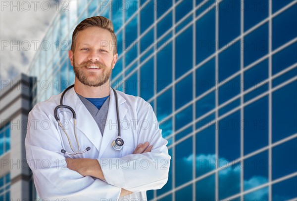 Handsome young adult male doctor with beard in front of hospital building