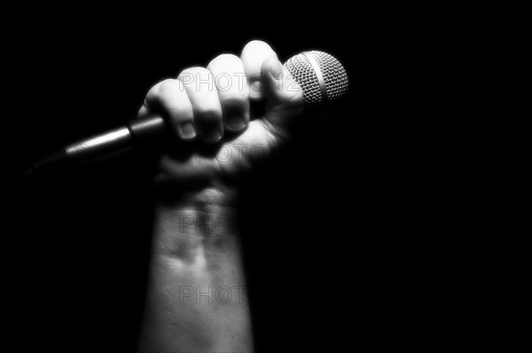 Grayscale microphone clinched firmly in male fist on a black background