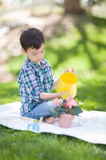 mixed-race young boy watering his potted flowers outside on the grass