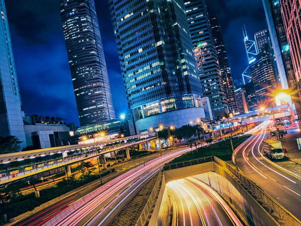 Street traffic in at night. Office skyscraper buildings and busy traffic on highway road with blurred cars light trails. Hong Kong