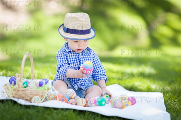 mixed-race chinese and caucasian baby boy outside wearing rabbit ears playing with easter eggs