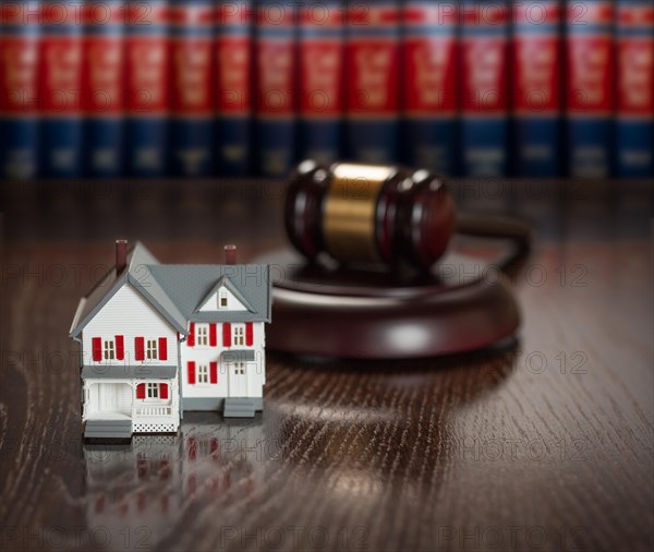 Gavel and small model house on wooden table with law books in background