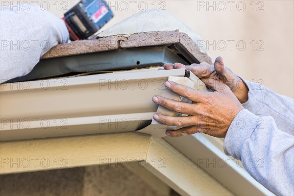 Worker attaching aluminum rain gutter to fascia of house