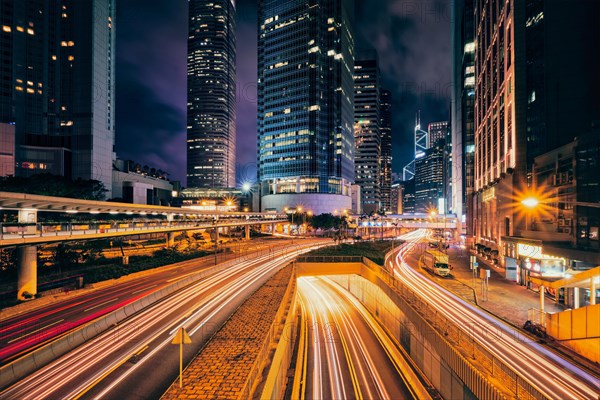 Street traffic in Hong Kong at night. Office skyscraper buildings and busy traffic on highway road with blurred cars light trails. Hong Kong