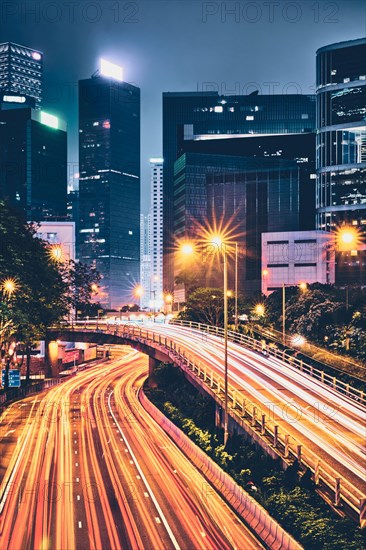 Street traffic in Hong Kong at night. Office skyscraper buildings and busy traffic on highway road with blurred cars light trails. Hong Kong