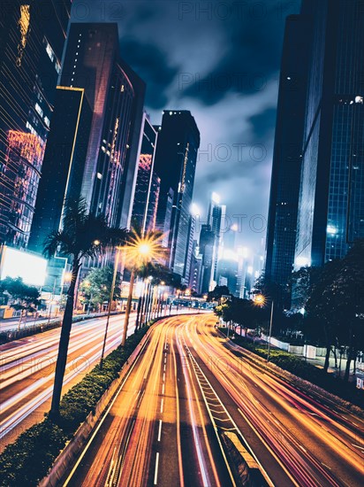 Street traffic in Hong Kong at night. Office skyscraper buildings and busy traffic on highway road with blurred cars light trails. Hong Kong