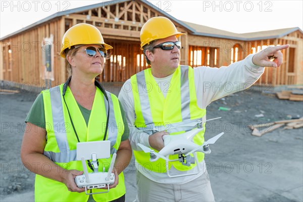 Workers with drone quadcopter inspecting photographs on controller at contruction site