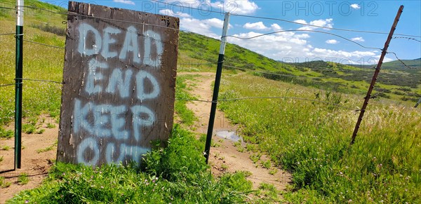 Dead end keep out sign on wire fence at dirt road