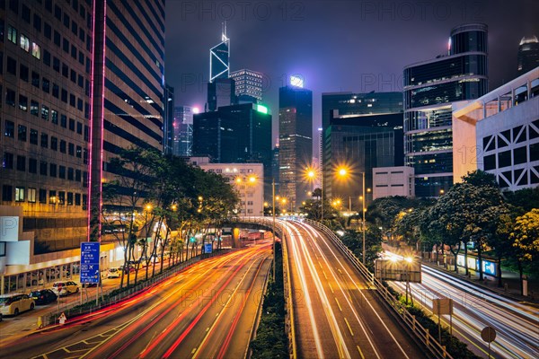 Street traffic in Hong Kong at night. Office skyscraper buildings and busy traffic on highway road with blurred cars light trails. Hong Kong