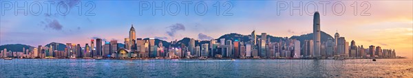 Panorama of Hong Kong skyline cityscape downtown skyscrapers over Victoria Harbour in the evening with junk tourist ferry boat on sunset with dramatic sky. Hong Kong