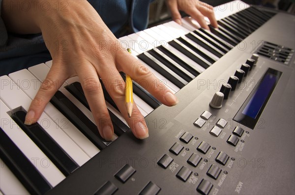 Woman's fingers with pencil on digital piano keys