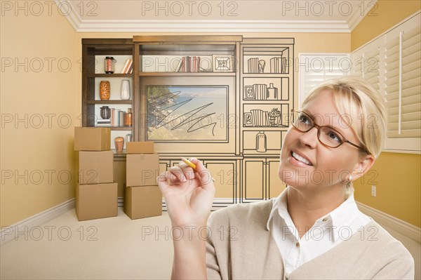 Female holding pencil in room with moving boxes and drawing of entertainment unit on wall