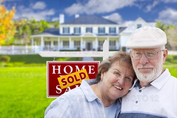 Happy affectionate senior couple hugging in front of sold real estate sign and house