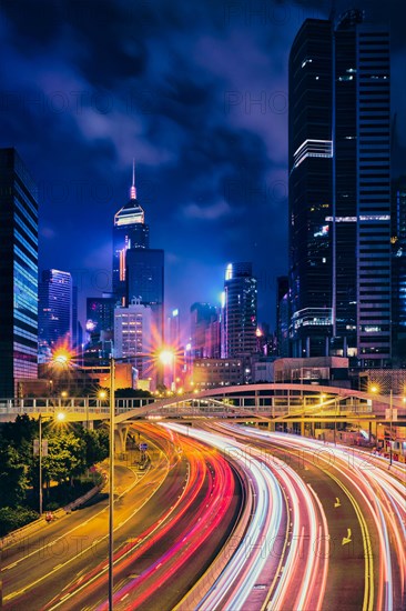 Street traffic in Hong Kong at night. Office skyscraper buildings and busy traffic on highway road with blurred cars light trails. Hong Kong