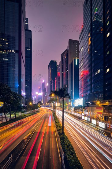 Street traffic in Hong Kong at night. Office skyscraper buildings and busy traffic on highway road with blurred cars light trails. Hong Kong