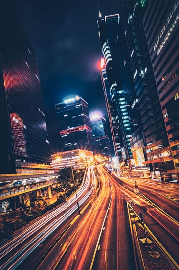 Street traffic in Hong Kong at night. Office skyscraper buildings and busy traffic on highway road with blurred cars light trails. Hong Kong